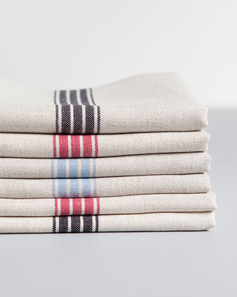Stack of Mungo provincial stripe napkins woven from cotton and linen with a colourful stripes, pictured here in french navy, red and bluebell
